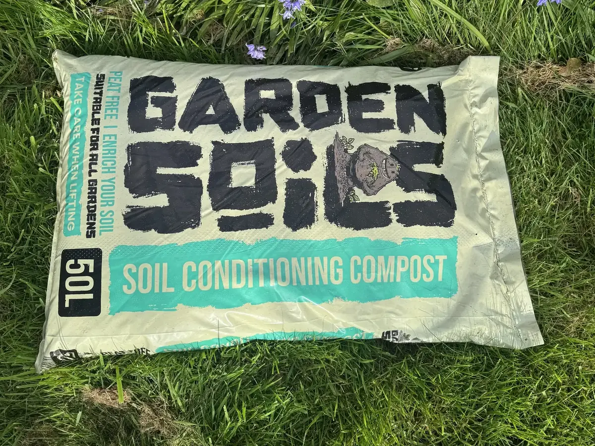 A 50L bag of Garden Soils peat-free compost in the grass by bluebells