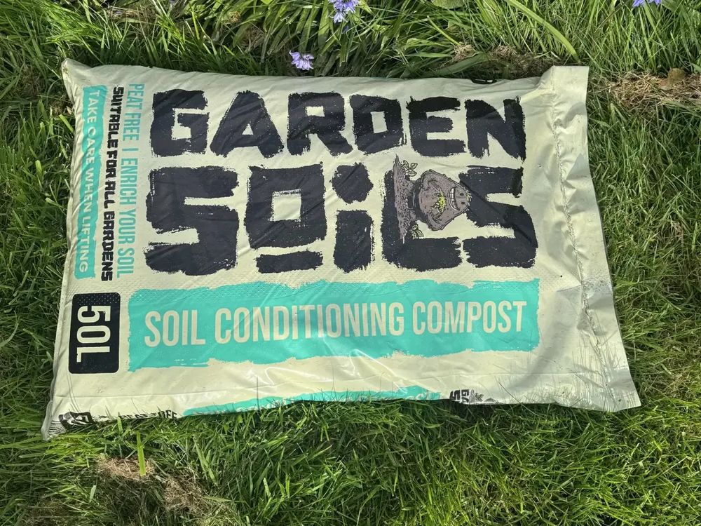 A 50L bag of Garden Soils compost in the grass by bluebells